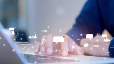 Hands typing on a laptop keyboard with digital icons nearby